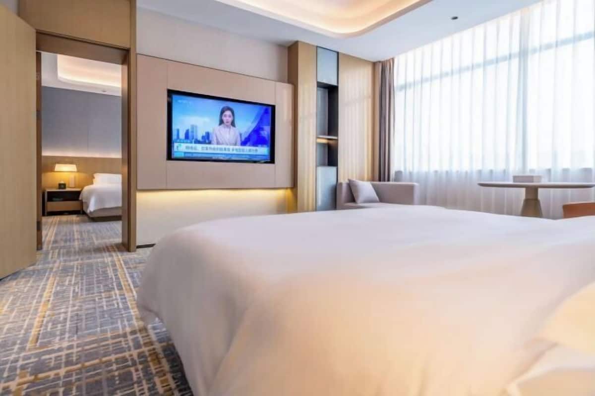 A modern hotel room with a large bed, a flat-screen TV mounted on the wall, a small table, and a chair.