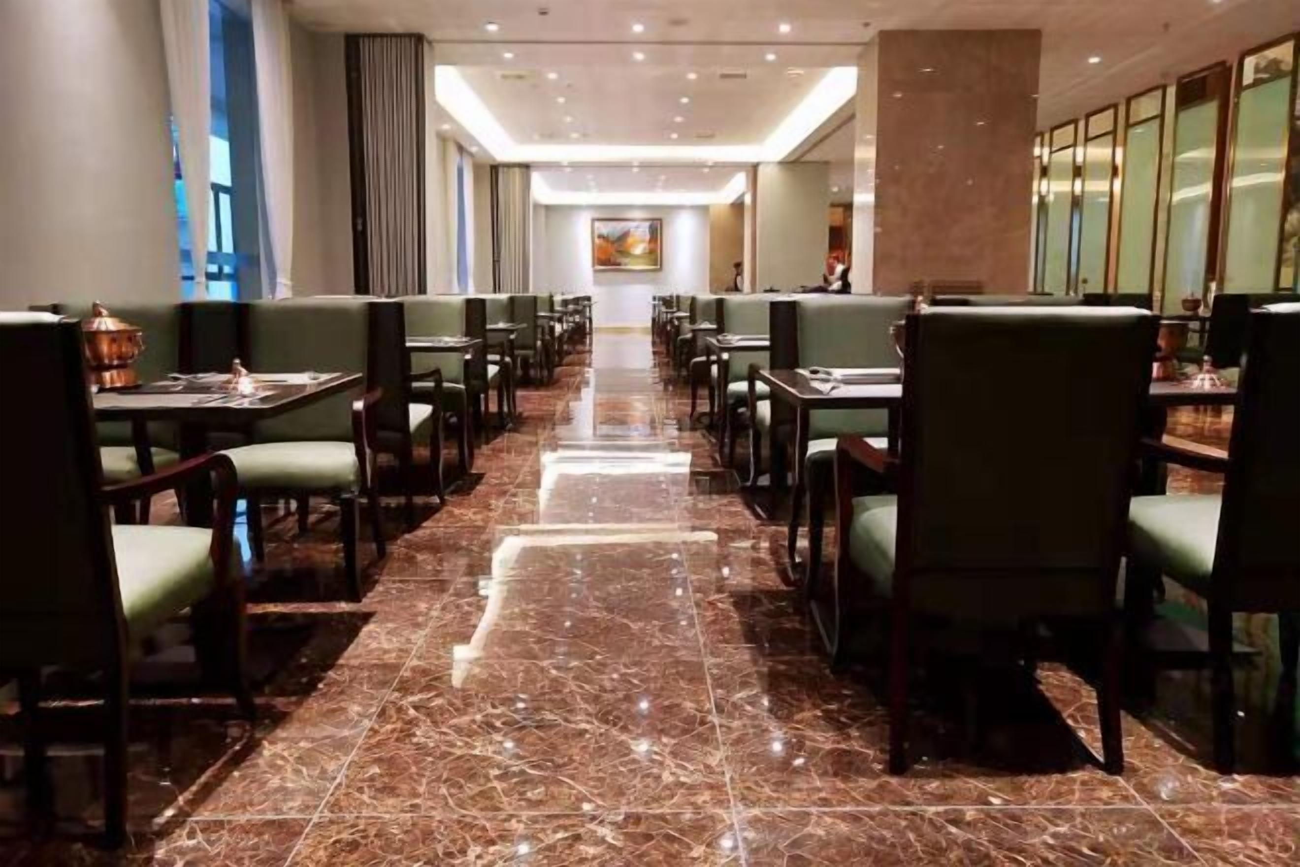 A spacious, well-lit restaurant with a long marble floor, green upholstered booths, and a central walkway.