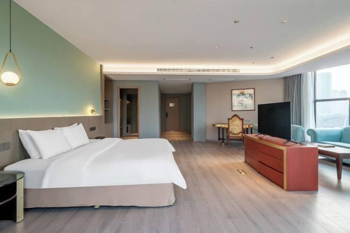 A modern hotel room with a large bed, a desk, a television, and a view of the city.