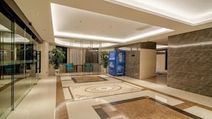 Un hall d’hôtel moderne avec un mur en verre, un comptoir d’accueil et un sol à motifs.