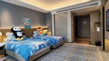 A hotel room with two beds, each with a penguin plush toy, a poster on the wall, and a TV on the right.