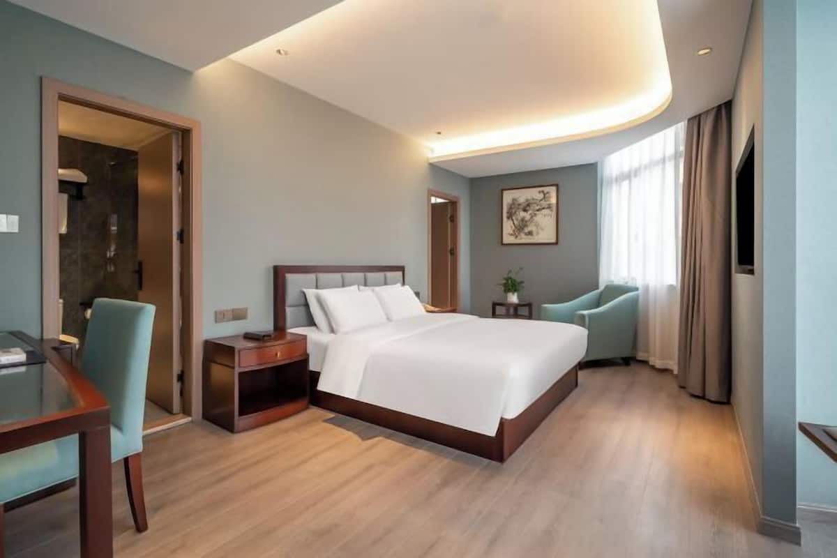 A hotel room with a large bed, a desk with a chair, a small table, and a TV.