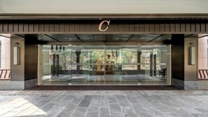 Une entrée d’hôtel moderne, avec une grande porte en verre, un logo en forme de « C » bien visible et une vue sur l’espace extérieur.