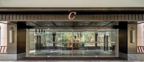 Una entrada de hotel moderna con un gran puerta de vidrio, un llamativo logo 'C' y vistas del área exterior.