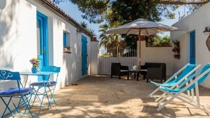 Een terras met blauwe stoelen, een tafel met een bloevas en een witte parasol.