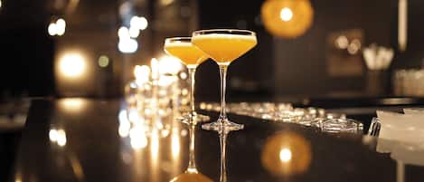 Dos vasos de martini con una bebida amarillenta sobre una barra reflectante.