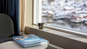 A book on a table by a window with a view of a snowy town. - The Tide - Hotel (Moskenes)
