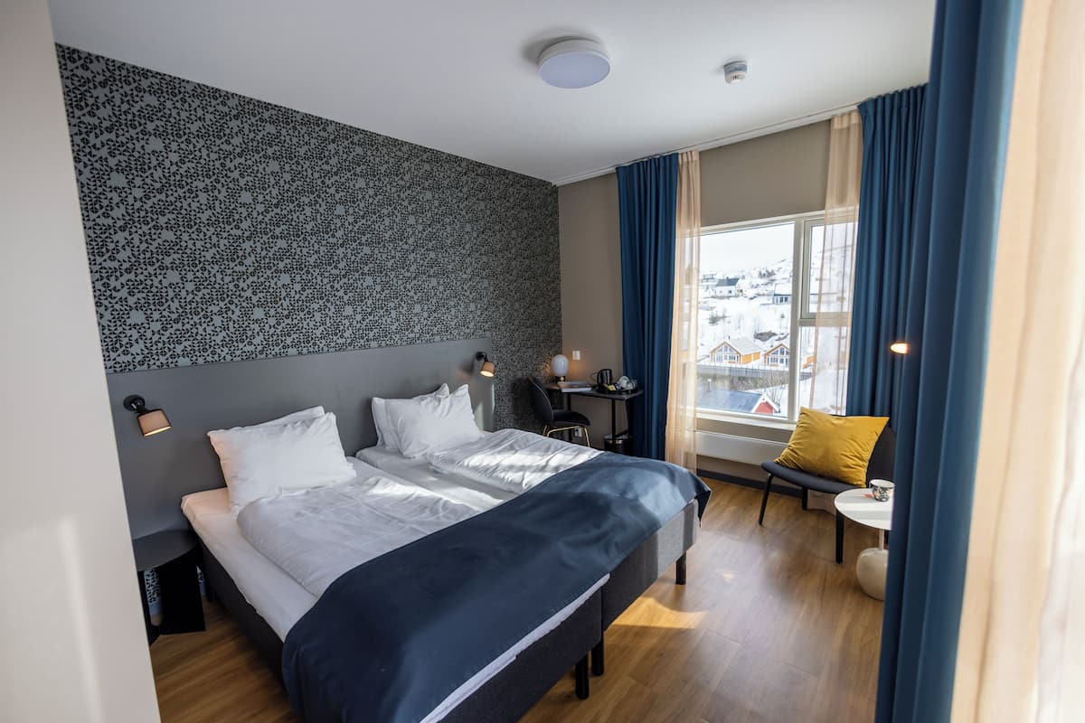 A modern hotel room with a large bed, a desk, and a chair.