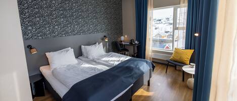 A modern hotel room with a large bed, a desk, and a chair.
