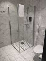 A modern bathroom with a glass-enclosed shower, a white toilet, and a tiled floor with a hexagonal pattern.