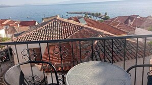 A balcony with a view of a coastal town, terracotta roofs, and a clear sky.