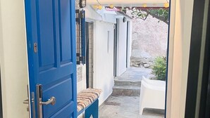 A hallway with a blue door leading to a covered outdoor area with a bench and a welcome mat.