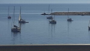 A coastal scene with multiple sailboats anchored near a rocky breakwater.