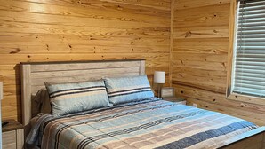 A wooden cabin bedroom with a bed, nightstands, a ceiling fan, and a window with blinds. - Rattletrap Cabin - 3bed/2bath (Scottsboro)