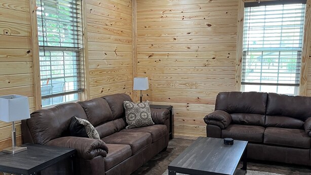 A cozy living room with wooden walls, two brown leather sofas, a coffee table, and a rug. - Rattletrap Cabin - 3bed/2bath (Scottsboro)