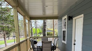 A covered porch with a wooden table and chairs, a door, and a window. - Rattletrap Cabin - 3bed/2bath (Scottsboro)