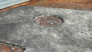 A concrete patio with a circular drain, surrounded by stone tiles, next to a house with blue siding and white trim. - Rattletrap Cabin - 3bed/2bath (Scottsboro)