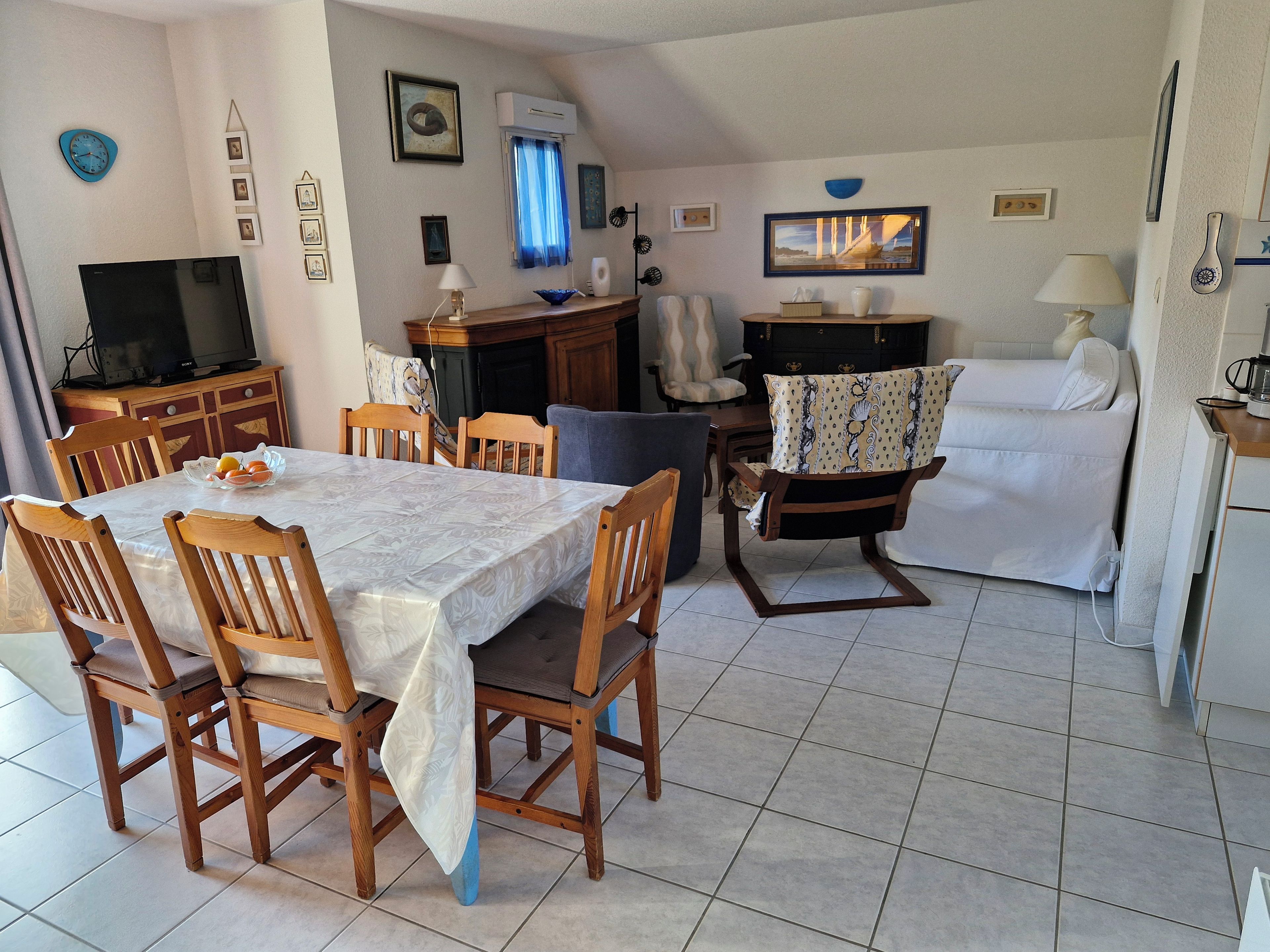 A dining area with a table and chairs, a television, and a kitchen area with a sofa and a coffee machine.