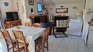 Un comedor con una mesa y sillas, un televisor y una zona de cocina con un sofá y una cafetera.