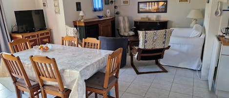 A dining area with a table and chairs, a television, and a kitchen area with a sofa and a coffee machine.