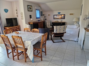Un comedor con una mesa y sillas, un televisor y una zona de cocina con un sofá y una cafetera.