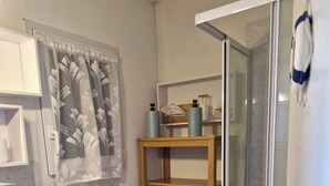 Un baño con tocador de madera, lavamanos blanco, cabina de ducha de vidrio y un perchero para toallas.