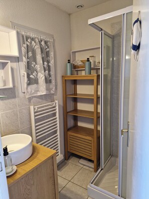 Un baño con tocador de madera, lavamanos blanco, cabina de ducha de vidrio y un perchero para toallas.