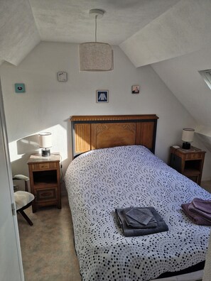 Un dormitorio con una cama, una mesita de noche, una silla y una pequeña mesa.