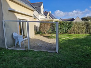 Um imóvel residencial com varanda coberta, uma cadeira de plástico branca e um jardim.