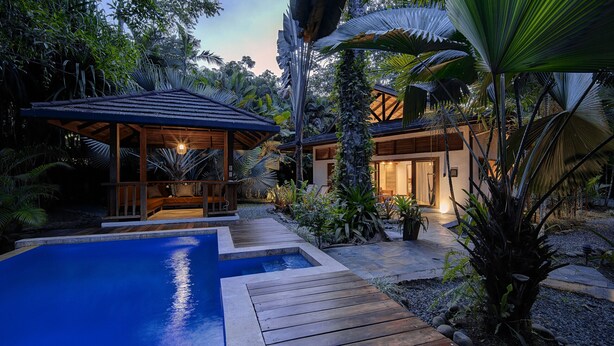 Ein Poolbereich mit Holzterrasse, umgeben von tropischen Pflanzen und einem Pavillon.