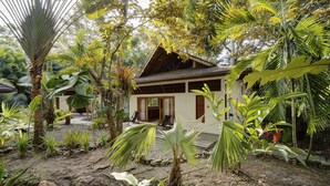 Een tropisch resort met een houten huis, omringd door weelderige begroeiing en palmbomen.