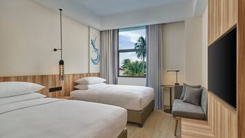 A hotel room with two beds, a sofa, a TV, and a window with a view of palm trees.