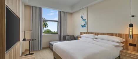 Una habitación de hotel moderna con una cama grande, un televisor de pantalla plana, una mesita de noche, una lámpara y vistas a palmeras.