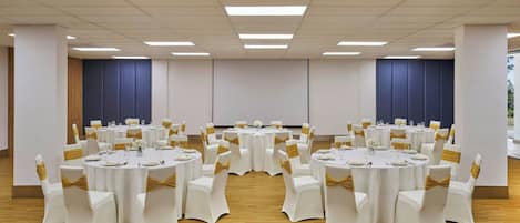 A conference room with round tables, white chairs with gold sashes, and a wooden floor.