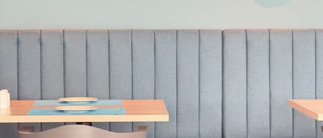 Un interior de restaurante con un asiento tapizado en azul, una mesa de madera con platos y un menú, y una silla de metal.