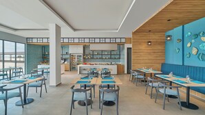 A modern restaurant with a long counter, multiple tables, and chairs. There is a kitchen area in the background. - Fairfield By Marriott Kuala Besut (Kampong Raja)