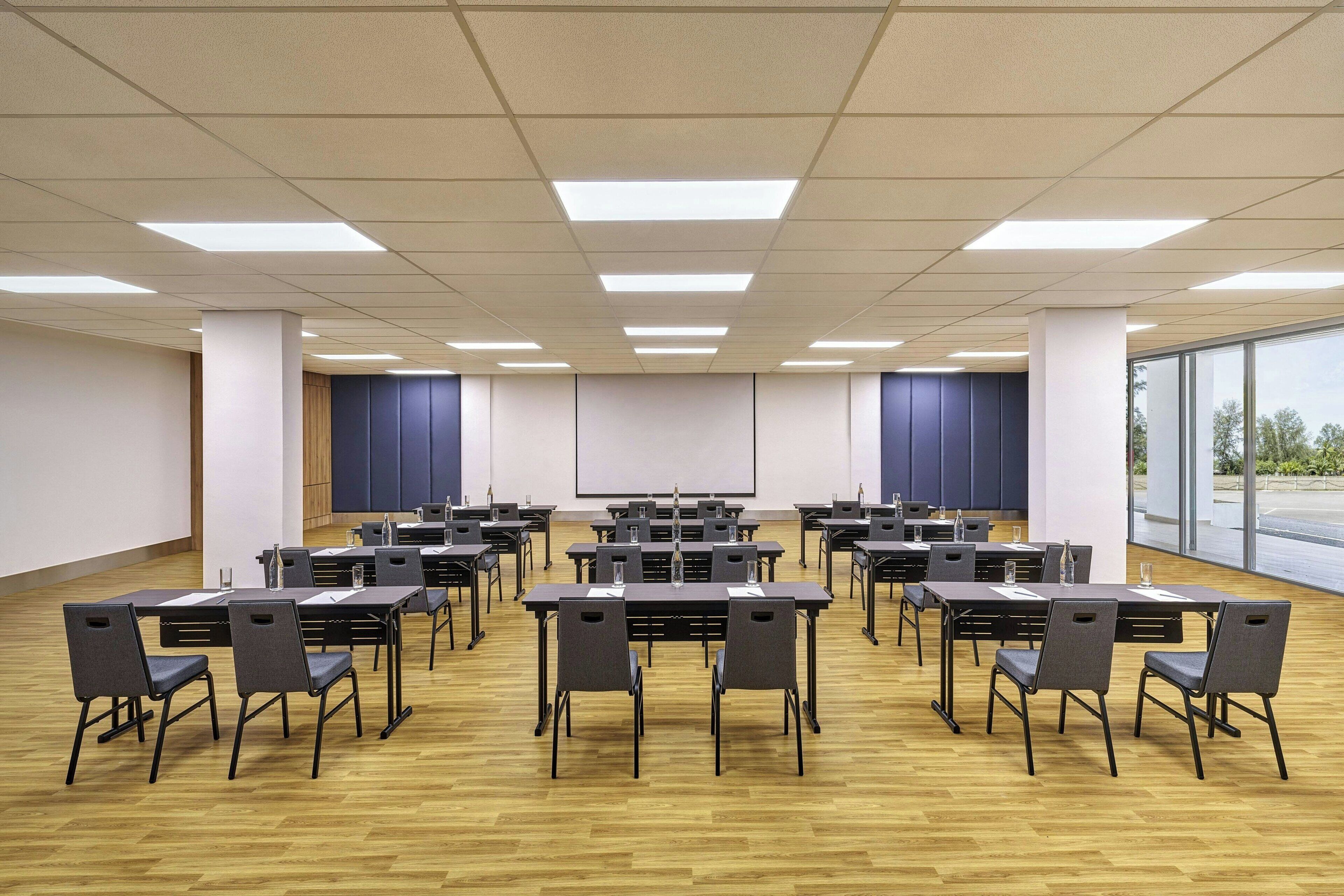 Una sala conferenze con diversi tavoli e sedie, ampie finestre e uno schermo per proiettore.