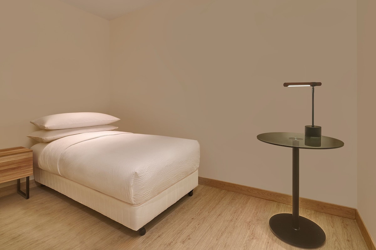 A bedroom with a bed, a bedside table, and a small round table with a lamp.