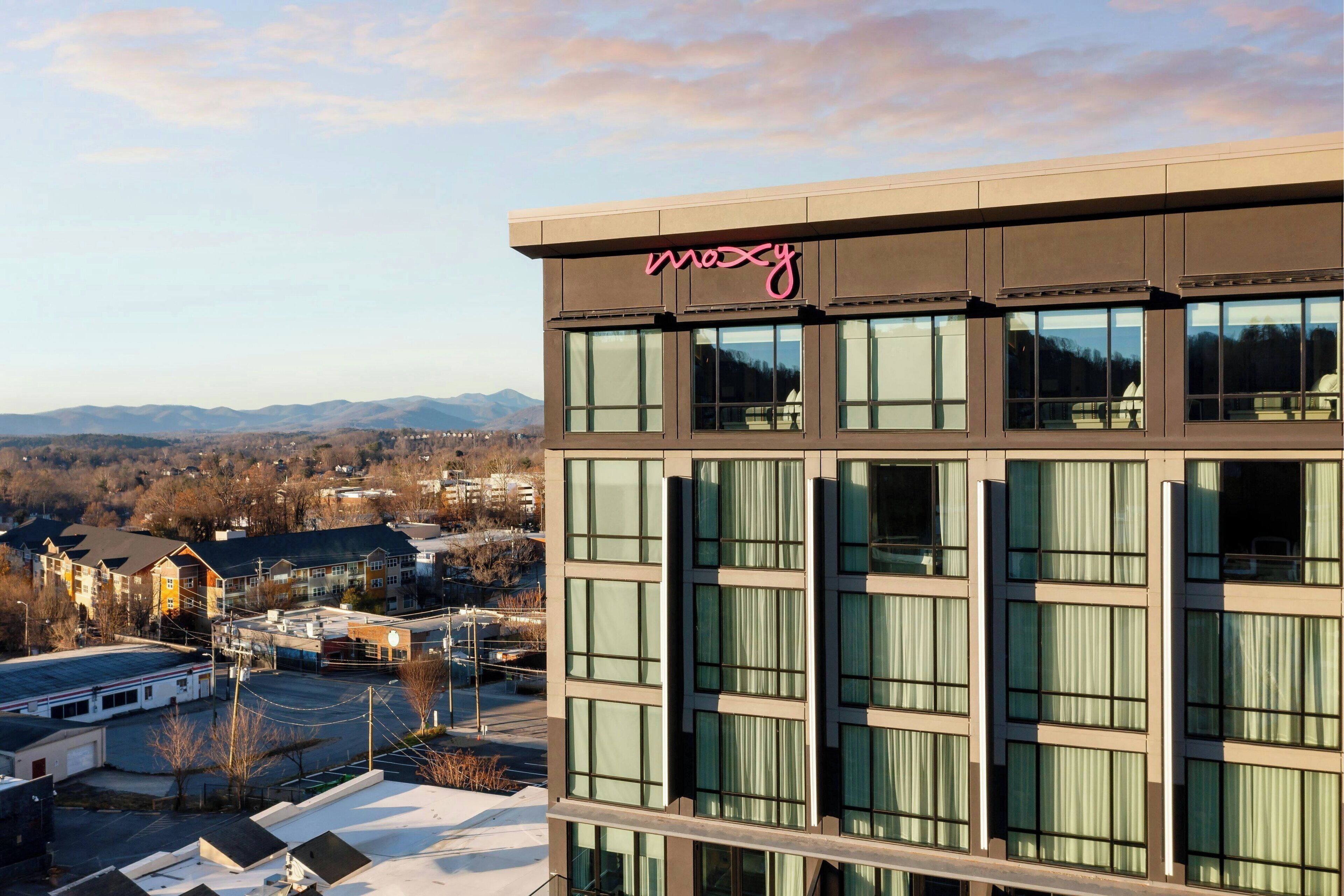 A modern building with a 'mozy' sign, large windows, and a view of a town and mountains in the background.