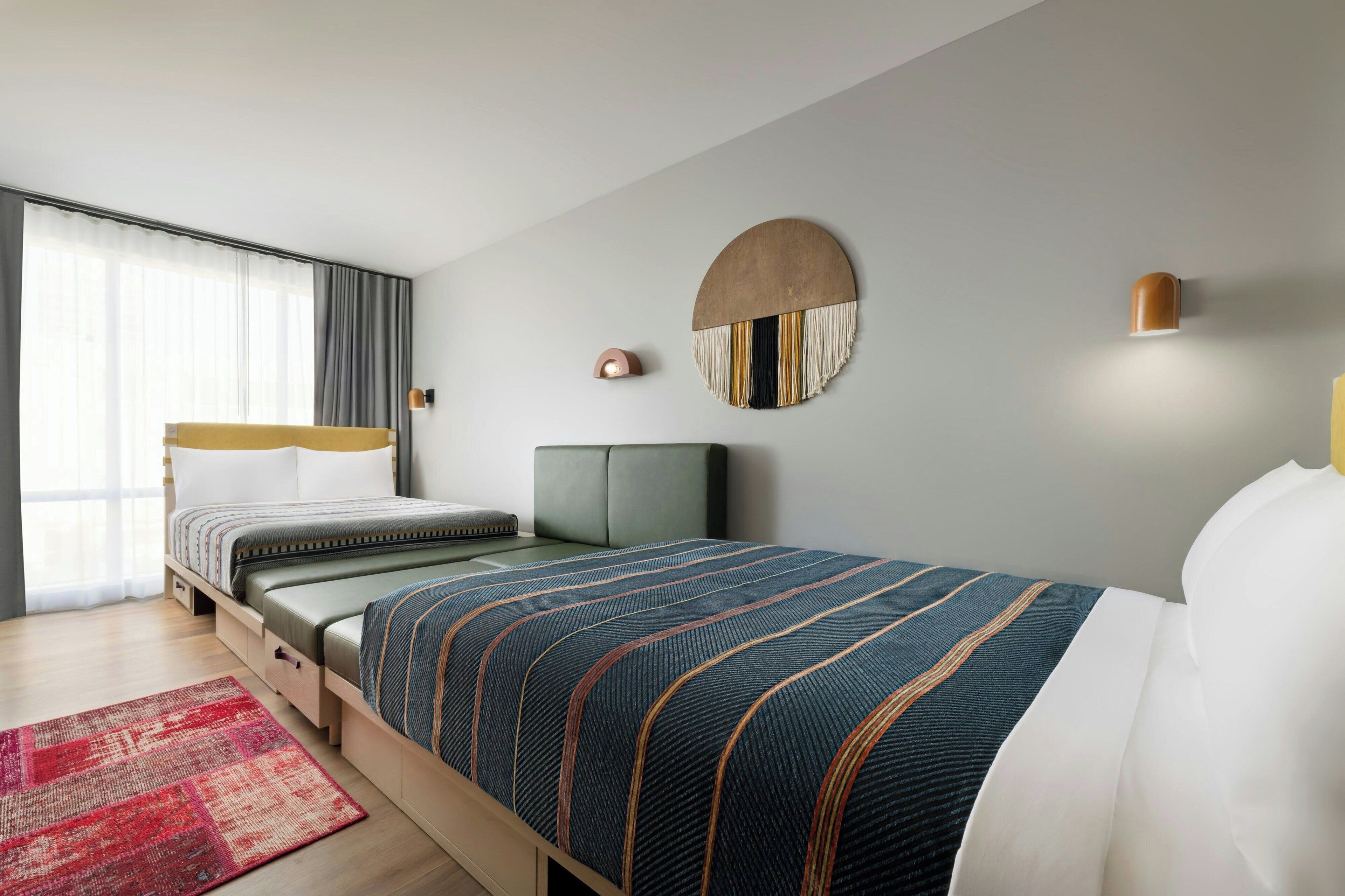 Une chambre d’hôtel moderne, équipée d’un lit, d’une table de chevet, d’une lampe, d’un élément de décoration circulaire fixé au mur et d’une fenêtre avec des rideaux.