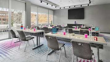 A conference room with large windows, multiple tables, and chairs, equipped with laptops and various office supplies.