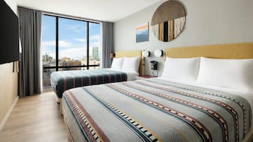 A hotel room with two beds, a large window with a city view, a round wall decoration, and a flat-screen TV.