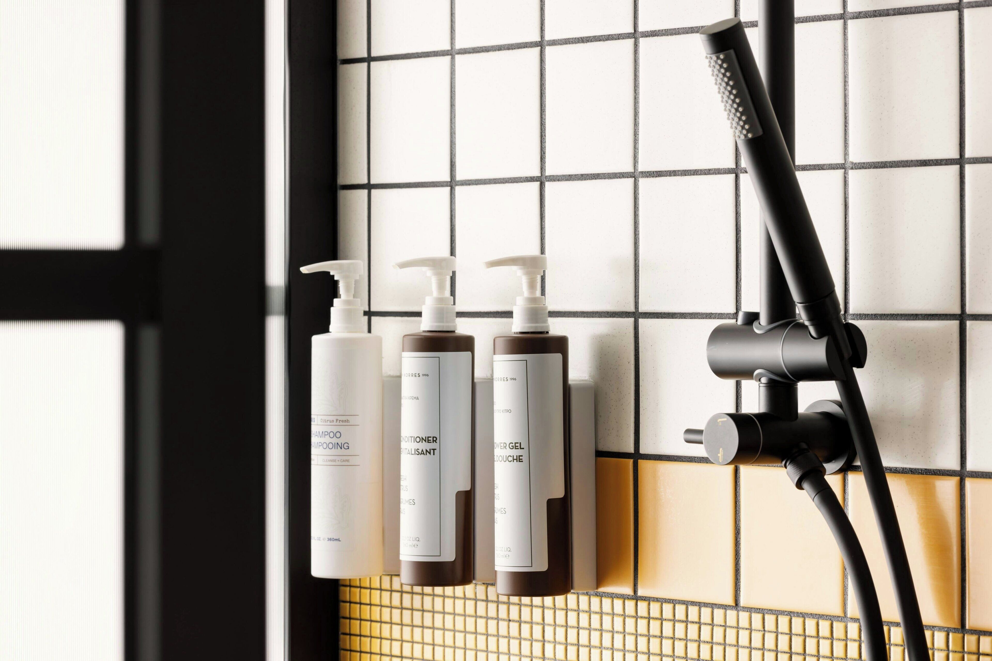 A bathroom with a shower, three bottles of toiletries, and a tiled wall.