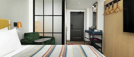 Una habitación de hotel moderna con una cama grande, un sofá verde, una mesita, un armario de madera, un espejo y un televisor.