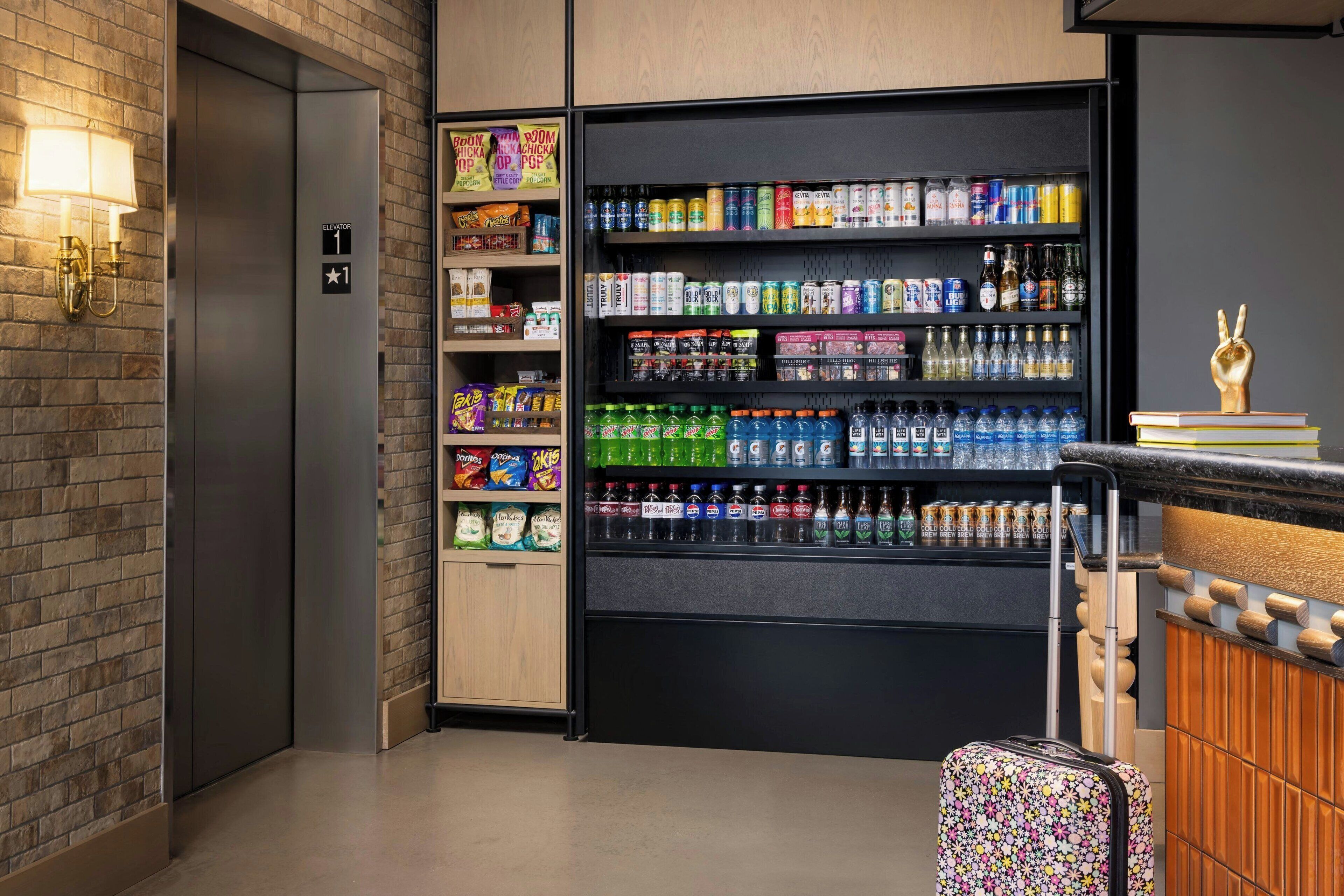 A vending machine with snacks and drinks, a luggage trolley, and a hand statue on a stack of books.