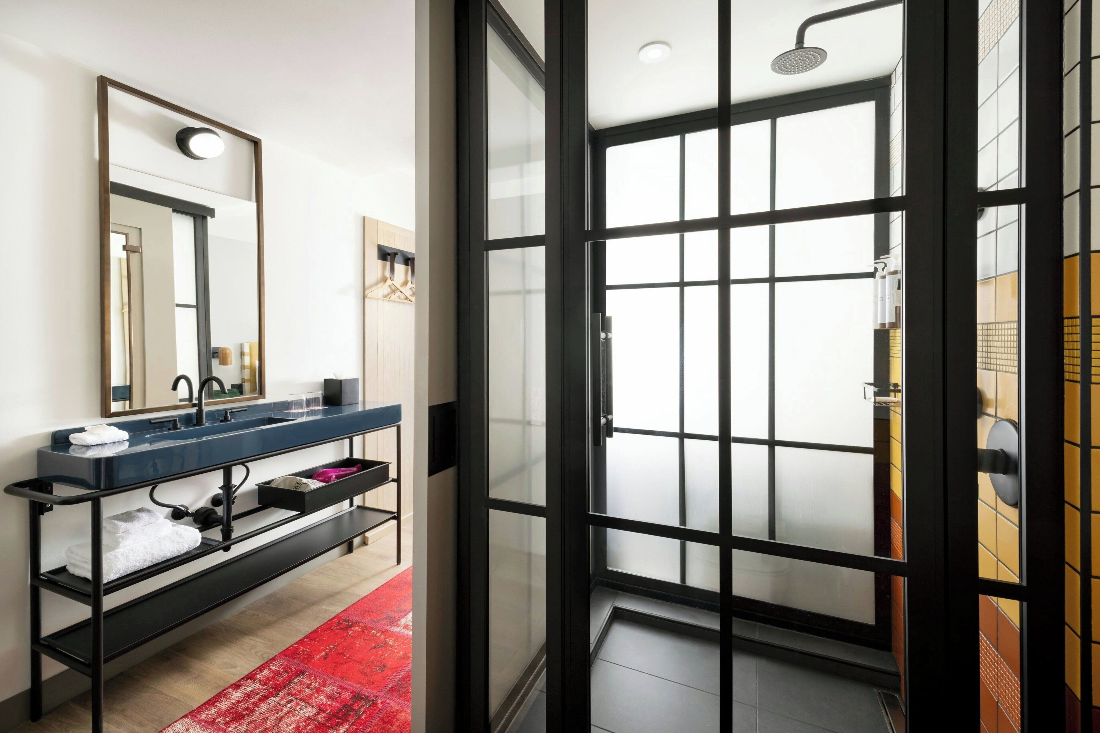 A modern bathroom with a glass shower enclosure, a black-framed mirror, and a blue countertop with a towel rack.