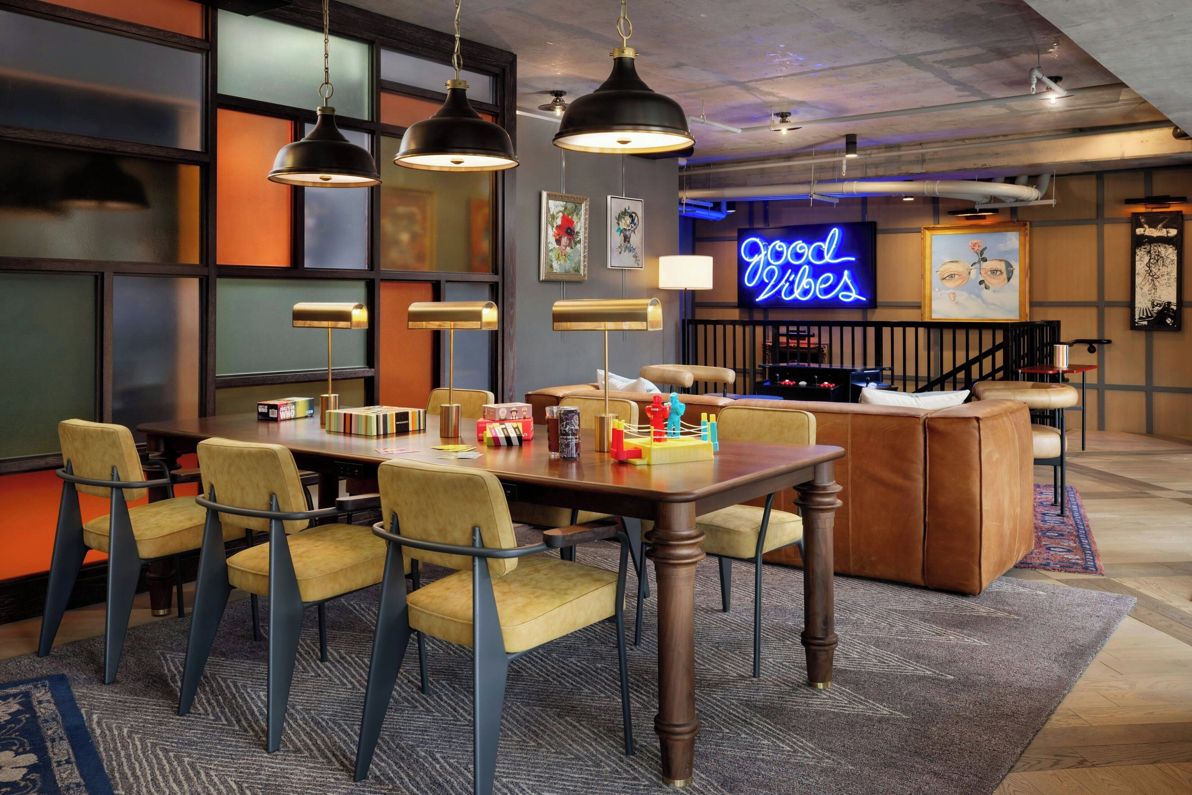 A modern dining area with a wooden table, yellow chairs, pendant lights, and a neon sign reading "Good Vibes".