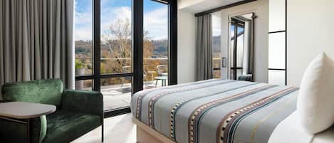 A modern hotel room with a large bed, a green sofa, a small table, and a view of the outdoors.