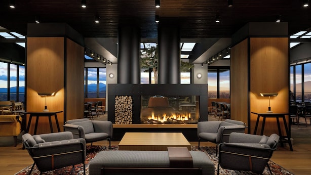 Un salon moderne doté d’une cheminée centrale, de sièges confortables et de grandes fenêtres offrant une vue sur les montagnes.