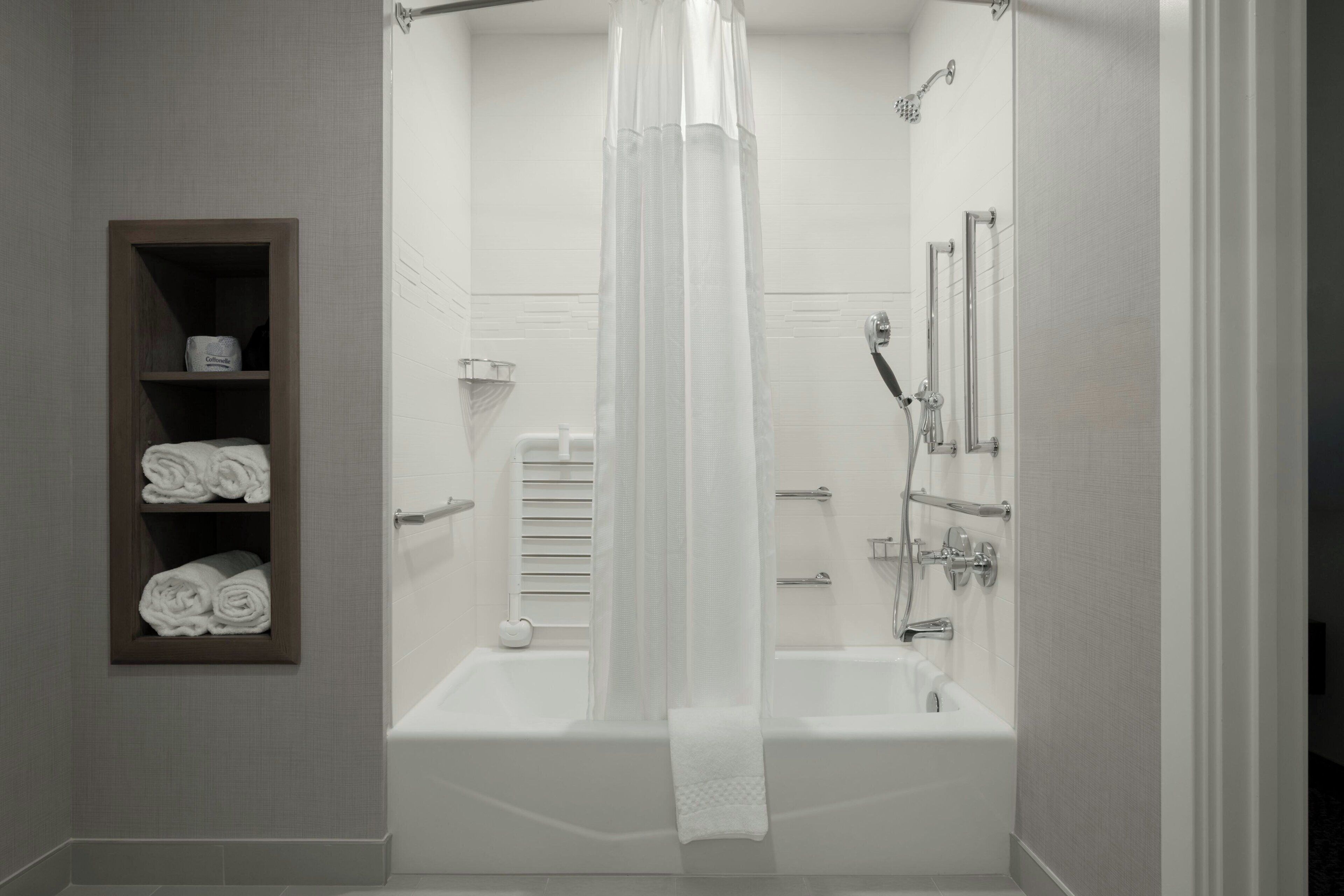 A modern bathroom with a bathtub, shower, and a shelf with towels.